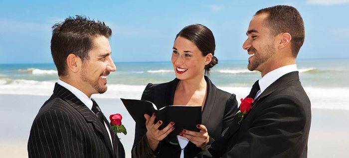 same sex relationship two men in black suits with red roses getting married on the beach woman marrying them