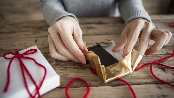 healthy valentine's day treats woman wrapping chocolate in a golden paper with red ribbon