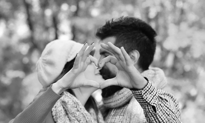 a couple making a heart with their hands and kissing black and white photo