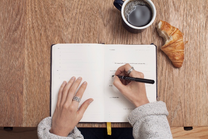 woman journaling on a table with a coffee and croissant 