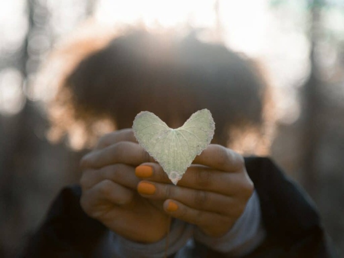 woman holding a heart shaped leaf in her hands with orange nail polish