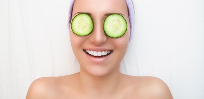 anti ageing plants woman smiling with cucumber slices on her eyes on a white background