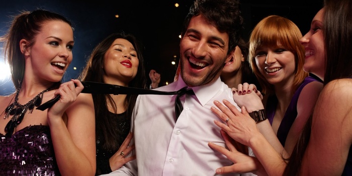 party man archetype smiling man with a white shirt and a tie surrounded by women in a bar