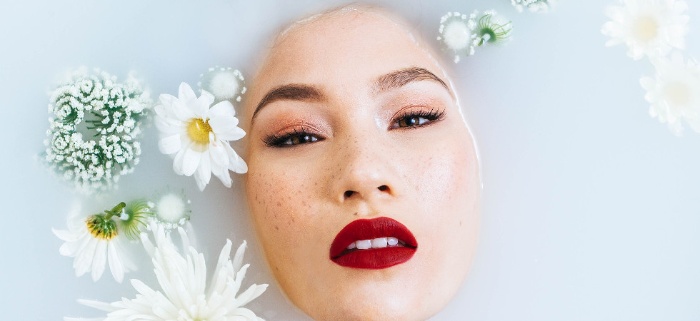asian woman with red lips in a white milky bath with flowers floating around her