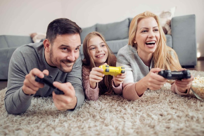 family of three mother daughter and father playing computer games lying on the floor