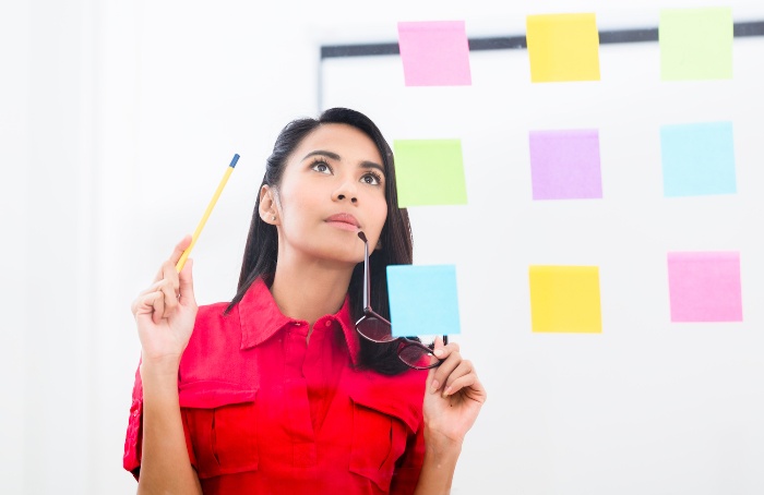 woman in red in front of a wall with colorful sticky notes holding her glasses