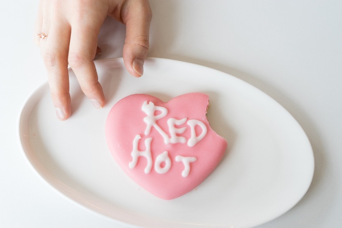 child's hand reaching for a heart shaped cookies with pink glazing and white writing