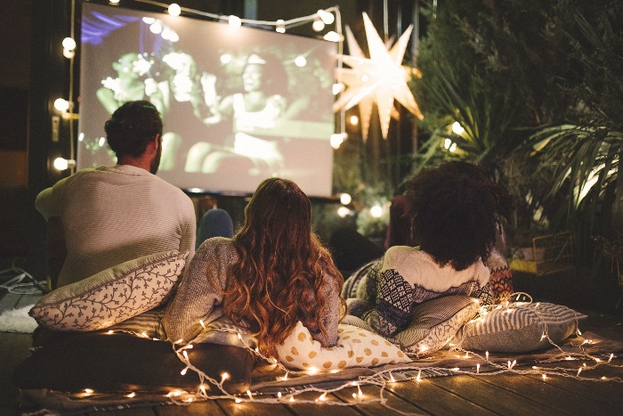 friends outdoors watching a movie on a big screen in a garden