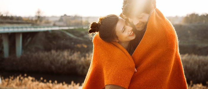 couple outdoors cuddling and smiling under an orange blanket