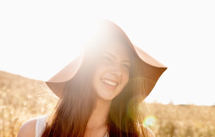 girl smiling outside in the sun wearing a wide hat 