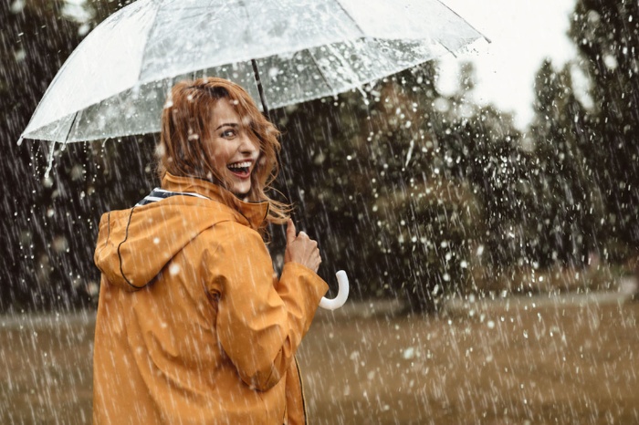 woman with an orange jacket smiling in the rain under a transparent umbrella