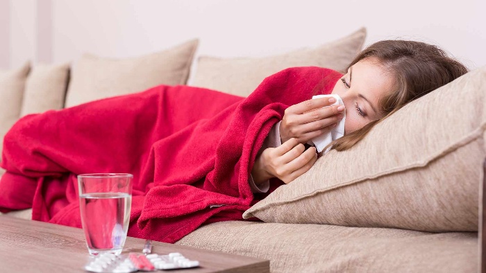 woman lying on a sofa covered with a red blanket sneezing 