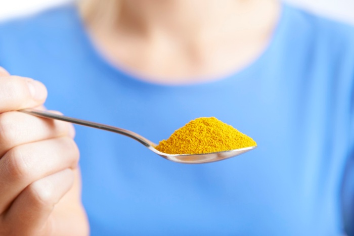 person with a blue shirt holding a spoon of turmeric