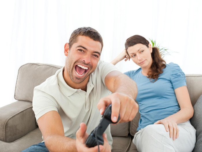 happy man playing video games woman sitting on the sofa next to him being bored
