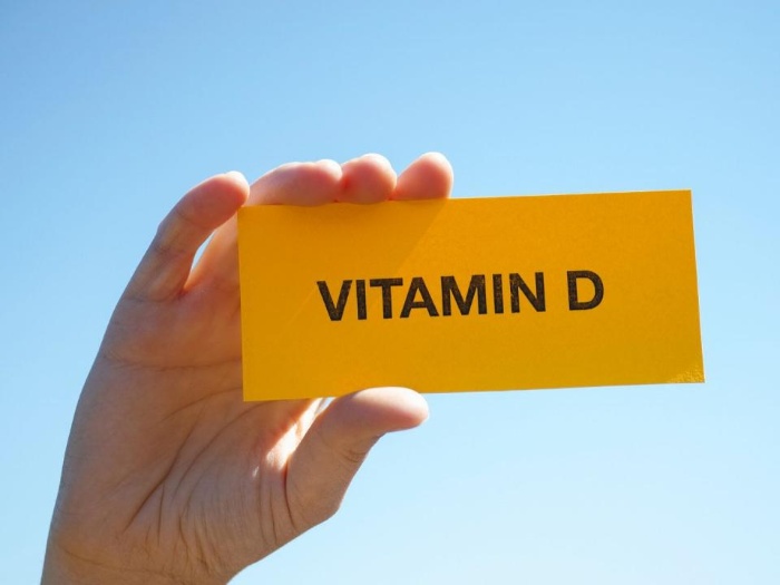 hand holding a yellow vitamin d sign on a blue background