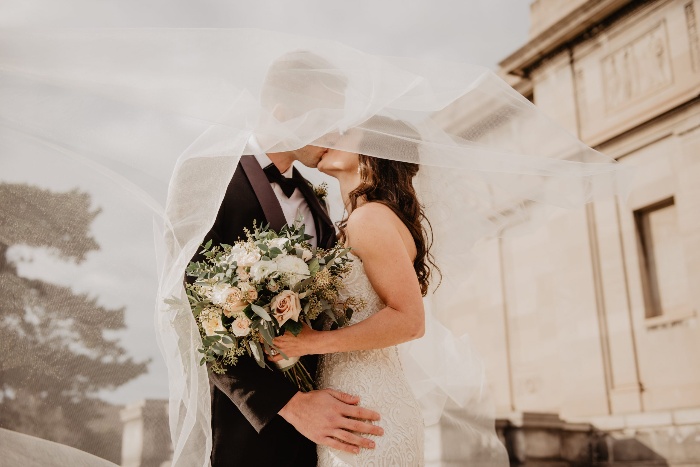 couple marrying kissing under a veil the bride is holding a bouquet