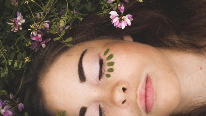 woman lying on the grass flowers around with green leaves under her eyes