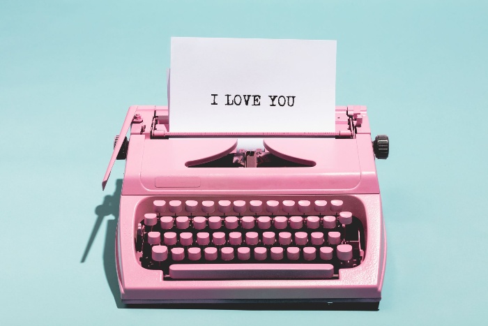  a pink typewriter with a white paper writing I love you