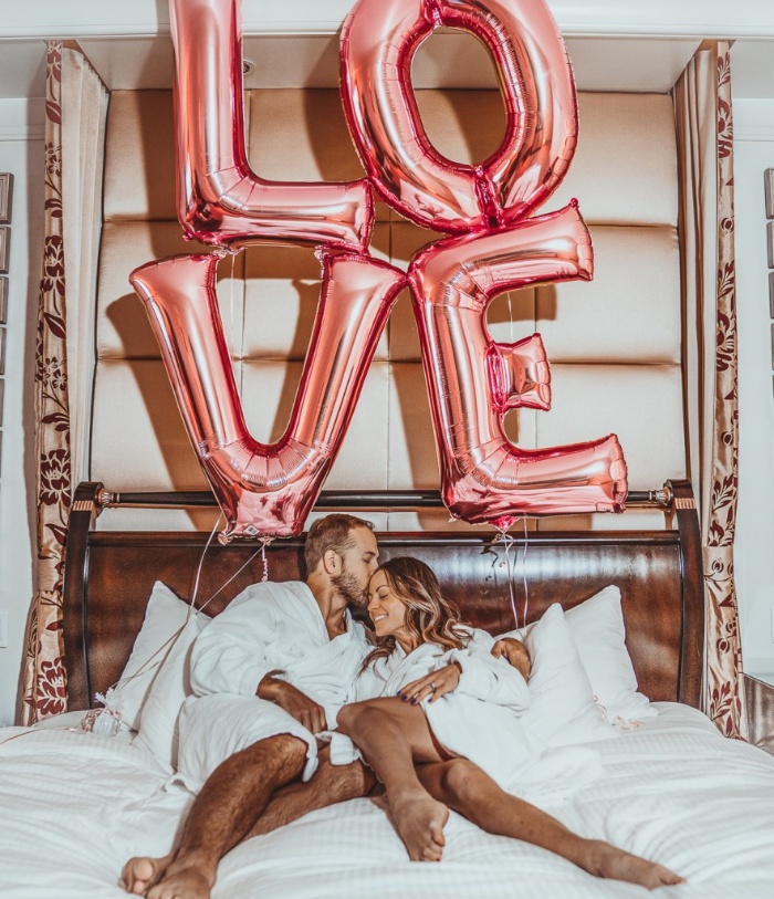 Pink Love balloons and a couple in a bed cuddling in white bathrobes 