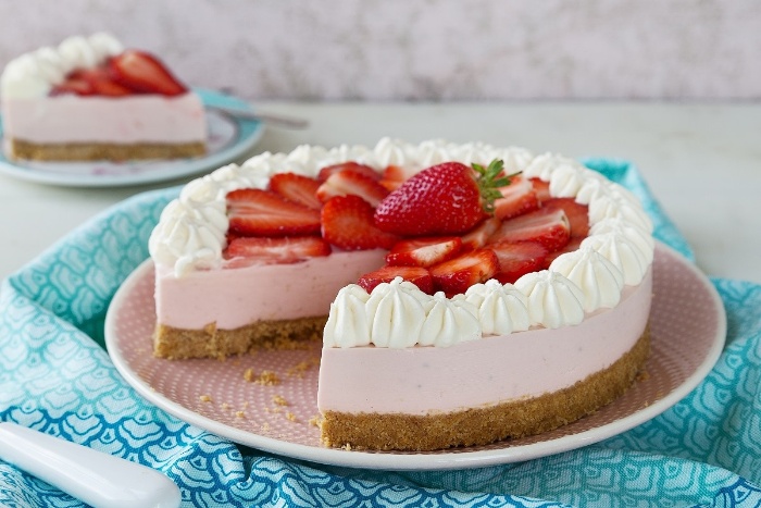unusual dessert spring pink cheescake with strawberries and cream crispy biscuit bottom on a blue cloth