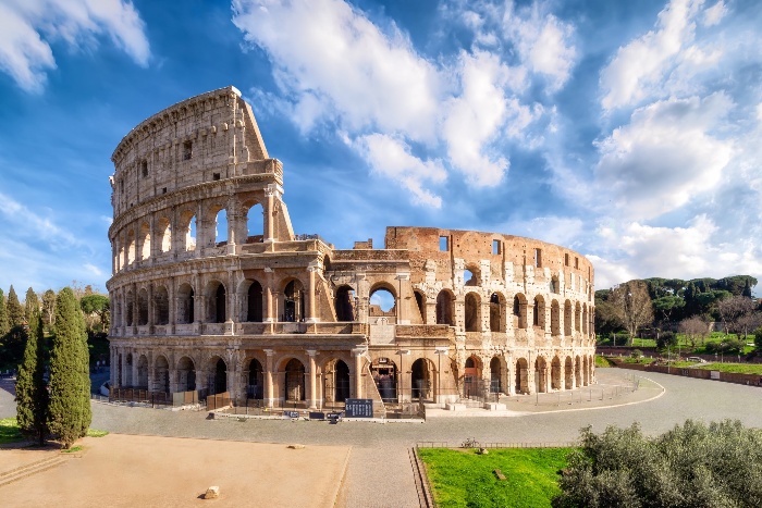 colloseum on a sunny day with clouds in the sky greenery around