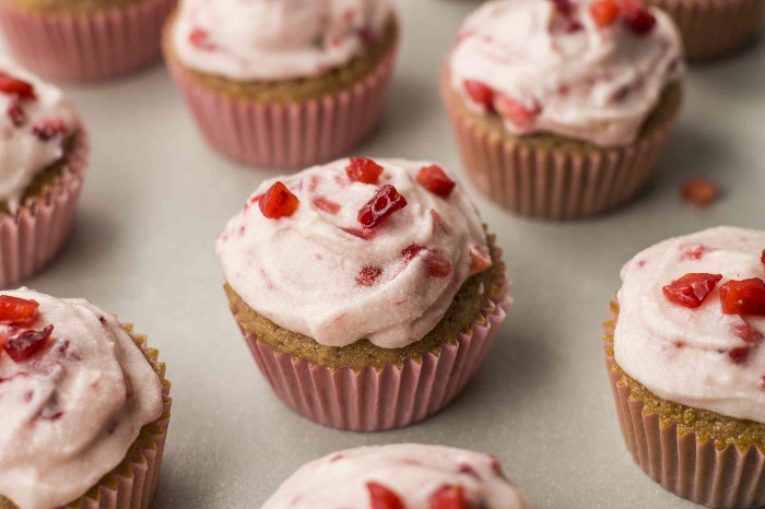 cupcakes with pink frosting and pieces of red berries on top in pink paper cups