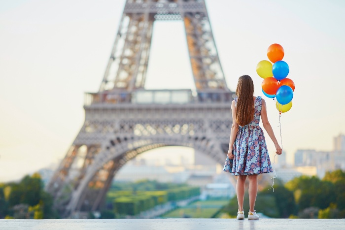 girl in a dress in front of the eiffel tower in Paris with colorful balloons in her hand