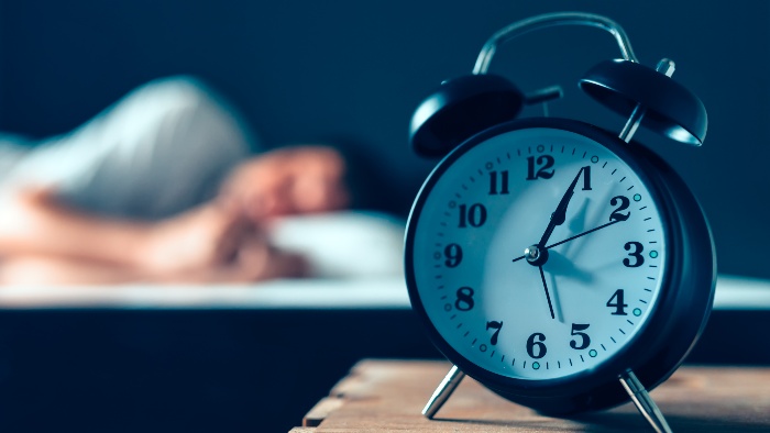 good sleep hours a table clock showing the time and a man sleeping in the background