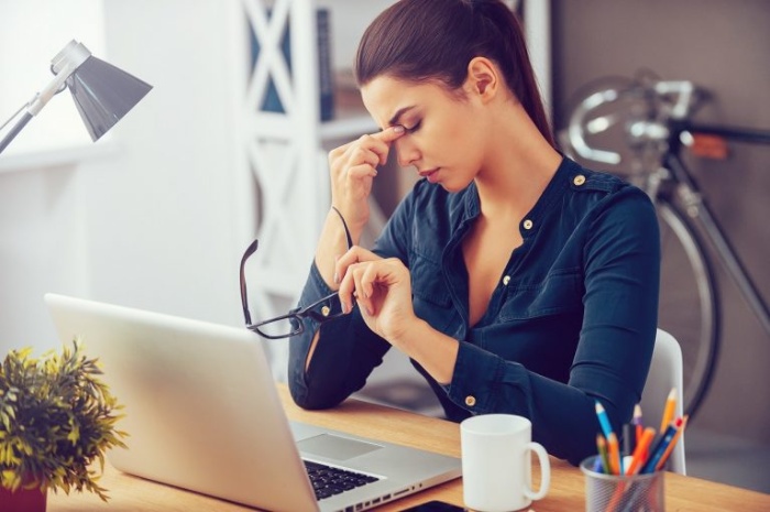 magnesium for health woman in dark blue shirt in front of her laptop holding her forehead with fingers