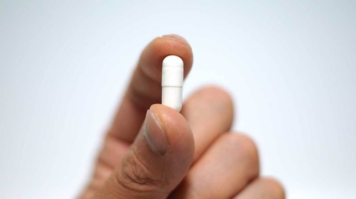 a hand holding a magnesium supplement pill between the fingers