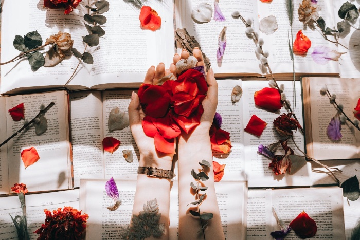 woman holding rose petals in her hands on the background of open books