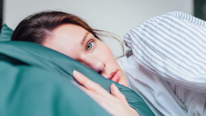 woman in bed with her eyes open looking at the camera