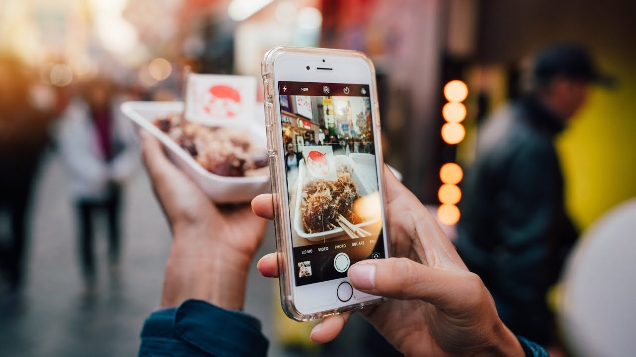 man taking a photo of their food with their phone on the street