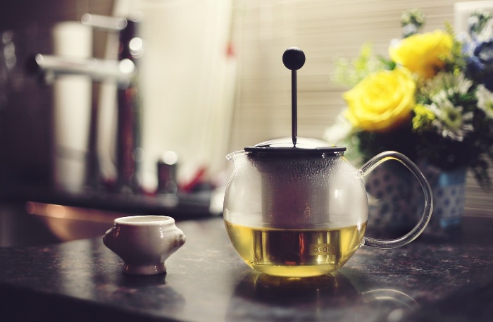 warm glass tea pot with a little cup on a kitchen table with flowers