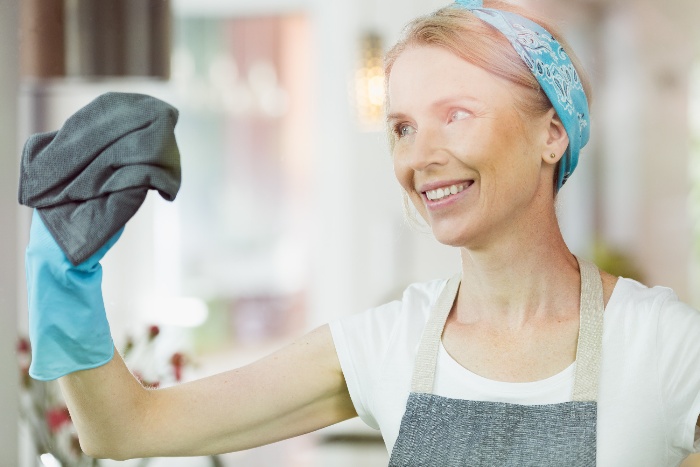 blond woman with blue headband and rubber gloves cleaning the windows with a gray cloth