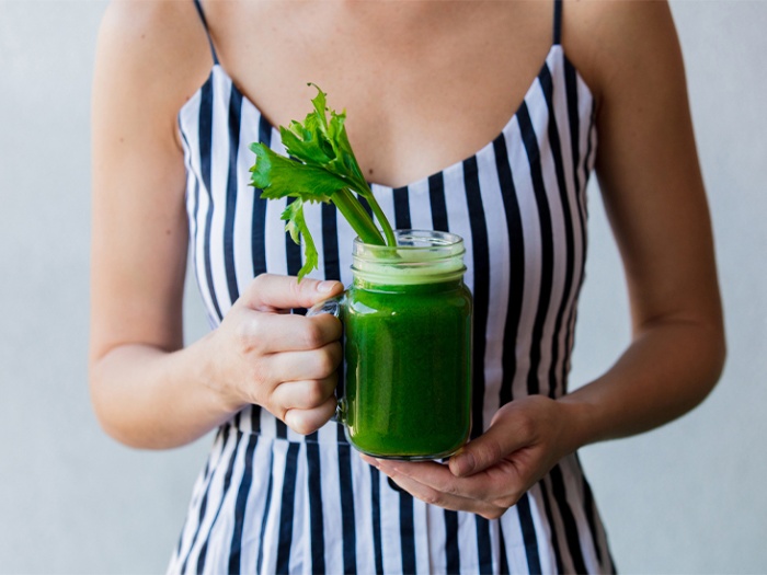 woman in striped dress holding a jar with green juice and celery sticking from it
