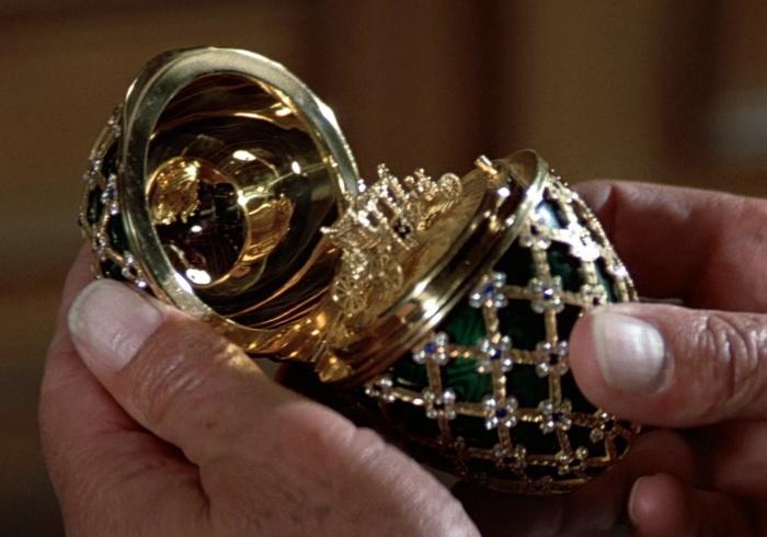 A hand holding an open a black and gold Faberge egg 