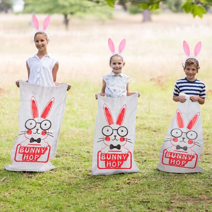 bunny hop race three children dressed like bunnies on a green lawn in bunny sacks ready to compete