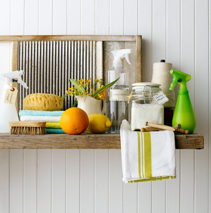 cleaning supplies on a wooden shelf on a white wall brushes towels lemon orange and sprays