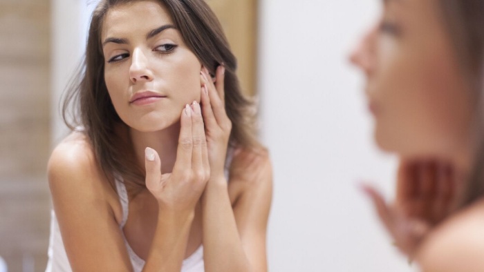 woman checking her skin in a mirror touching with her hands