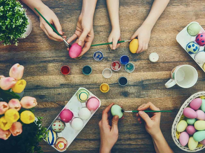 hands dying and painting easter eggs on a wooden table with brushes and paint