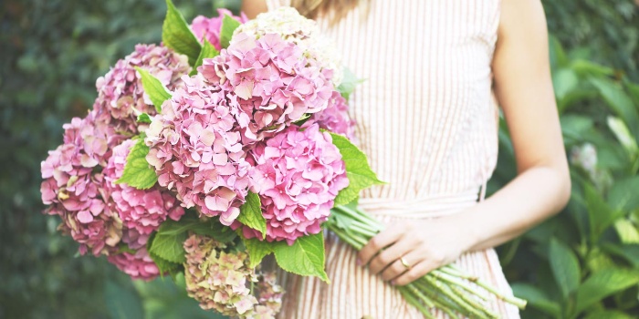 woman in a beige dress holding a large bouquet of pink flowers 