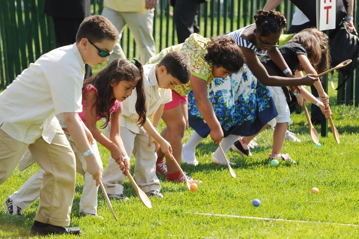 egg roll children with wooden spoons rolling eggs on a green lawn