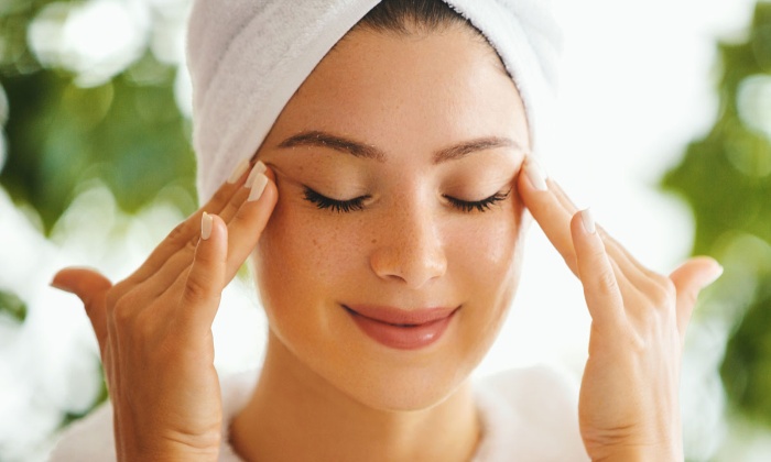 woman with white towel on her head outdoors enjoying a calming facial massage with her eyes closed