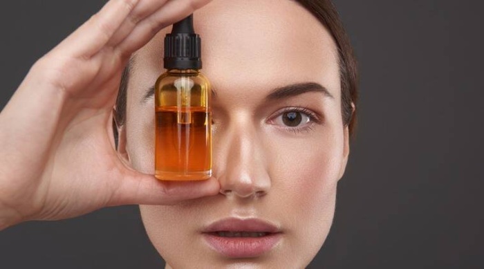 woman holding a light brown small bottle of skin oil in front of her eye