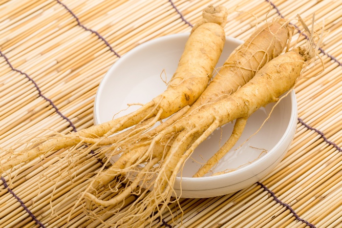 three gingseng roots in a white bowl on a hay table cover