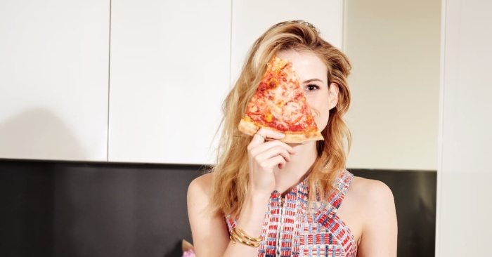girl holding a piece of pizza in front of her eye in the kitchen