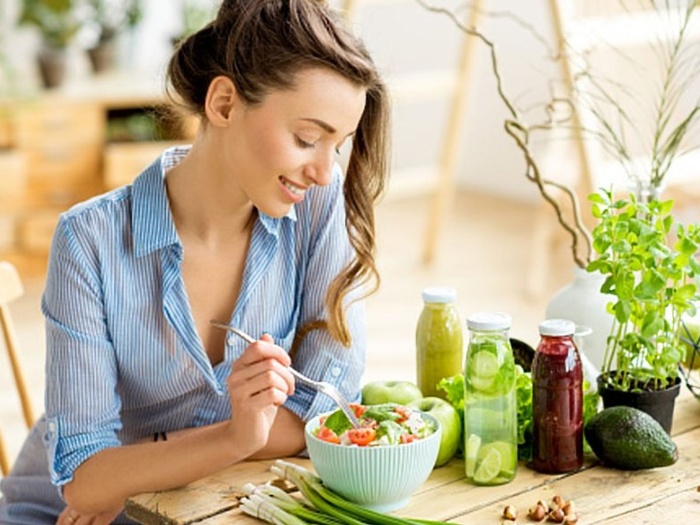 girl eating salad and smiling on a table with other vegetables and juices