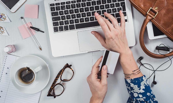 money tips woman with a card in her hand writing on a laptop on her desk with a cup of coffee and glasses