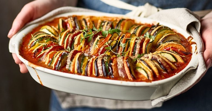 woman holding a tray with delicious ratatuille vegan meal freshly made out of the oven 